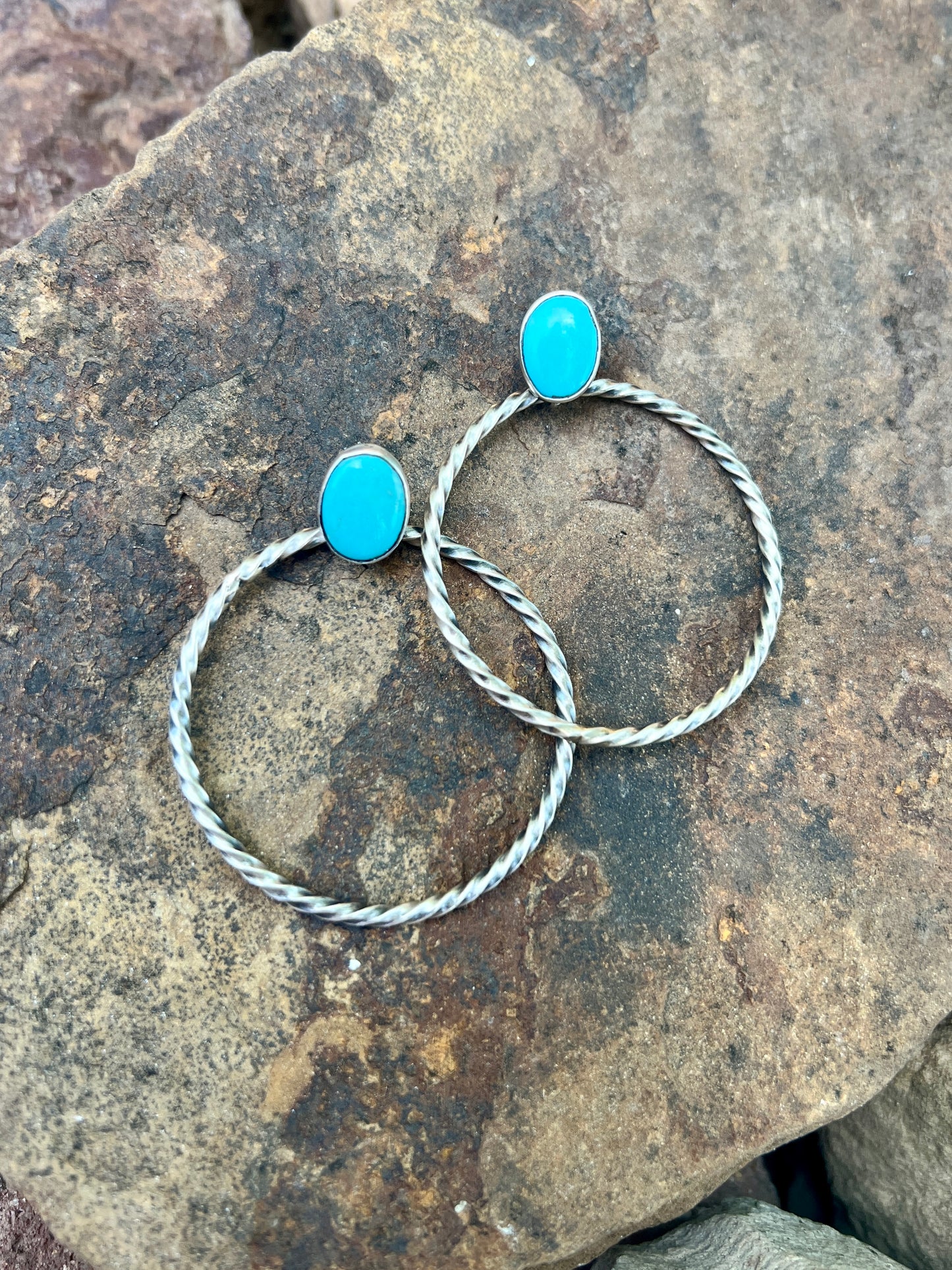 Two silver hoop earrings with turquoise stones on a rocky surface
