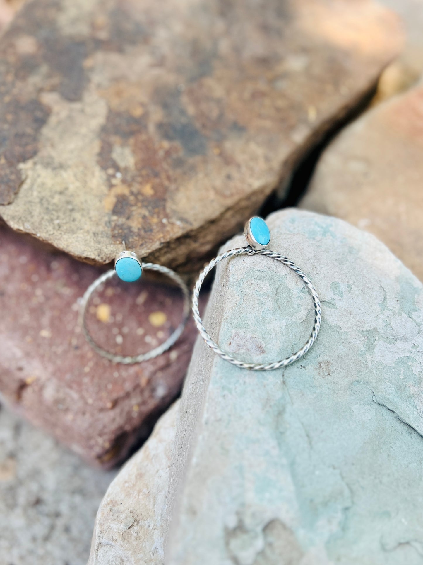 Silver hoop earrings with turquoise stones on a stone surface