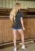 Woman standing in a barn wearing a dark denim shirt and shorts.