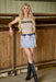 Woman wearing a 'Cowgirl' tank top and denim skirt standing in a barn.