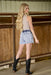 Woman in denim shorts and studded boots standing in a stable.