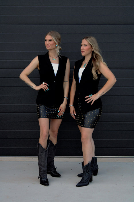 Two women in matching black outfits standing against a black background