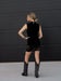 Woman wearing a black sleeveless top and skirt standing against a black wall.
