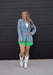 Woman wearing a denim jacket, green shorts, and white cowboy boots against a black background