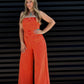 Woman wearing an orange jumpsuit against a black slatted wall.
