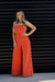 Woman wearing an orange jumpsuit against a black slatted wall.