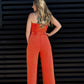 Woman wearing a bright orange jumpsuit standing against a black slatted wall.