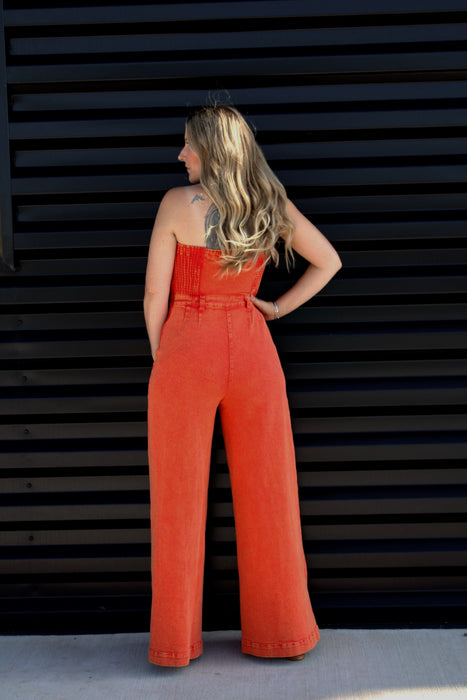 Woman wearing a bright orange jumpsuit standing against a black slatted wall.