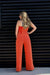 Woman wearing a bright orange jumpsuit standing against a black slatted wall.