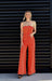 Woman wearing a bright orange strapless jumpsuit against a black slatted wall.