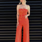 Woman wearing an orange jumpsuit standing against a black slatted wall.
