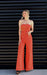 Woman wearing an orange jumpsuit standing against a black slatted wall.