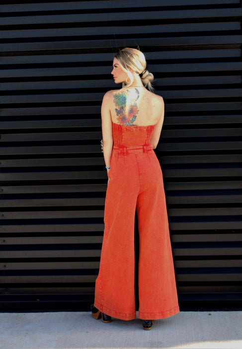 Woman wearing an orange jumpsuit against a black slatted wall.