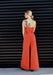 Woman wearing an orange jumpsuit against a black slatted wall.
