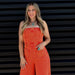 Woman wearing an orange jumpsuit standing against a black slatted wall.