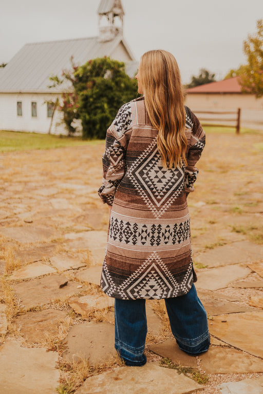 Person wearing a patterned cardigan standing on a stone path with a church in the background
