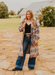 Woman in a patterned coat and jeans standing on a stone path outdoors.