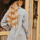 Woman wearing a denim jacket and black hat in front of a rustic wooden wall.
