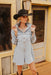 Woman wearing a denim dress and cowboy hat in front of a wooden building.