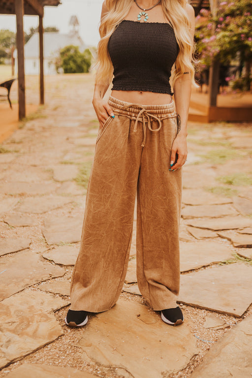 Person wearing a black crop top and tan wide-leg pants on a stone path.