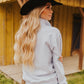 Woman wearing a black cowboy hat and light gray jacket outdoors.