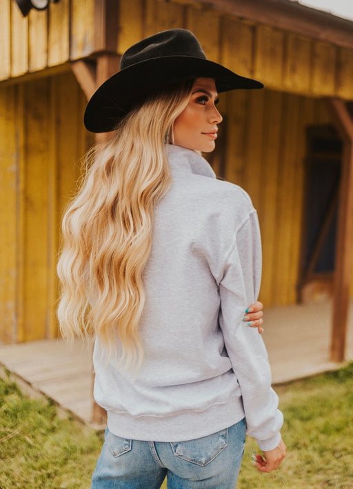 Woman wearing a black cowboy hat and light gray jacket outdoors.