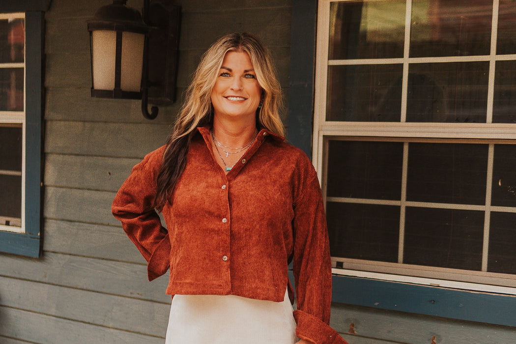 Woman in a red suede jacket and white skirt standing on a wooden deck.