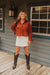 Woman in a red suede jacket and white skirt standing on a wooden deck.
