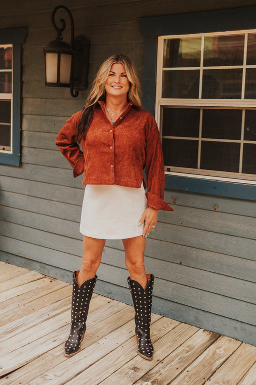 Woman in a red suede jacket and white skirt standing on a wooden deck.