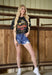 Woman wearing a black t-shirt with a graphic design and denim shorts in a barn setting