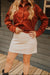 Person wearing a rust-colored button-up shirt and beige skirt standing on a wooden deck.