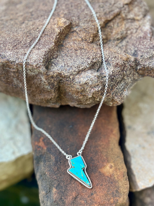 Necklace with a blue lightning bolt pendant on a stone surface