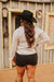 Person wearing a black cowboy hat and light shirt standing in front of a wooden building.