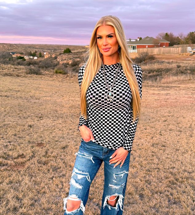 Woman wearing a black and white checkered shirt and ripped jeans standing in an open field.