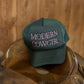 Green cap with 'Modern Cowgirl' text on a leather horse bridle against a wooden background
