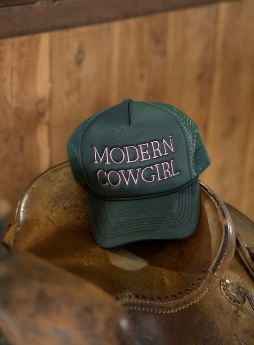 Green cap with 'Modern Cowgirl' text on a leather horse bridle against a wooden background