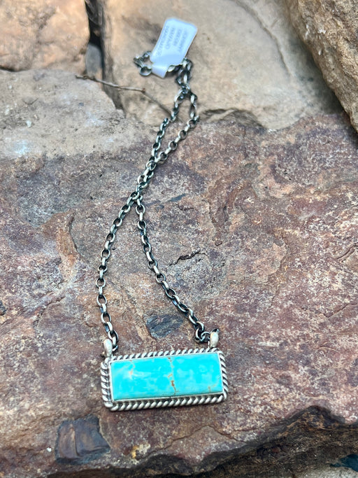 Turquoise pendant necklace on a chain on a rocky surface