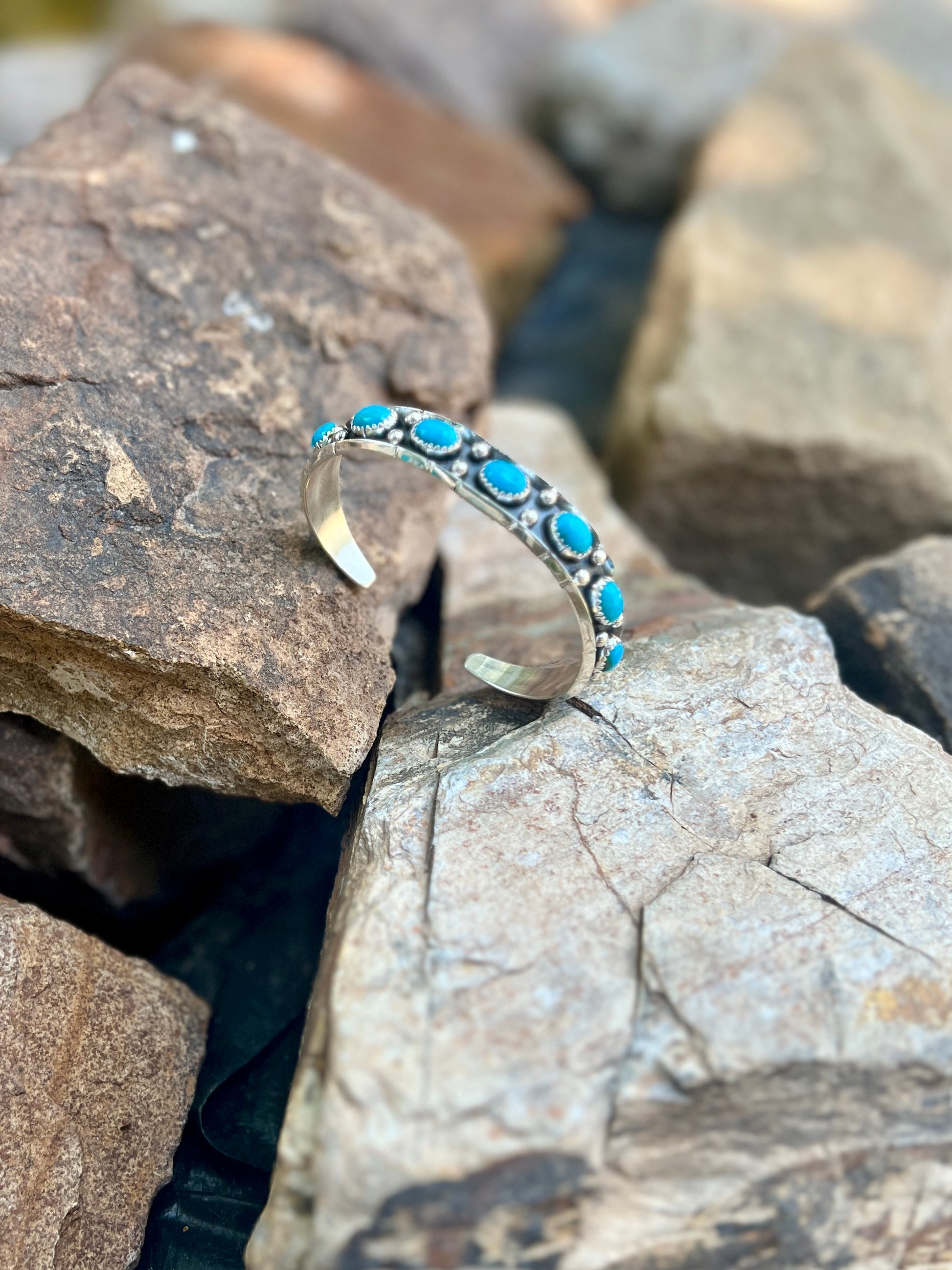 Silver bracelet with turquoise stones on a rocky surface