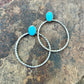 Two silver hoop earrings with turquoise stones on a rocky surface