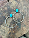 Two silver hoop earrings with turquoise stones on a rocky surface