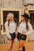 Two women in western attire standing in front of a wooden building.