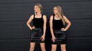 Two women wearing black outfits with studded details against a black background