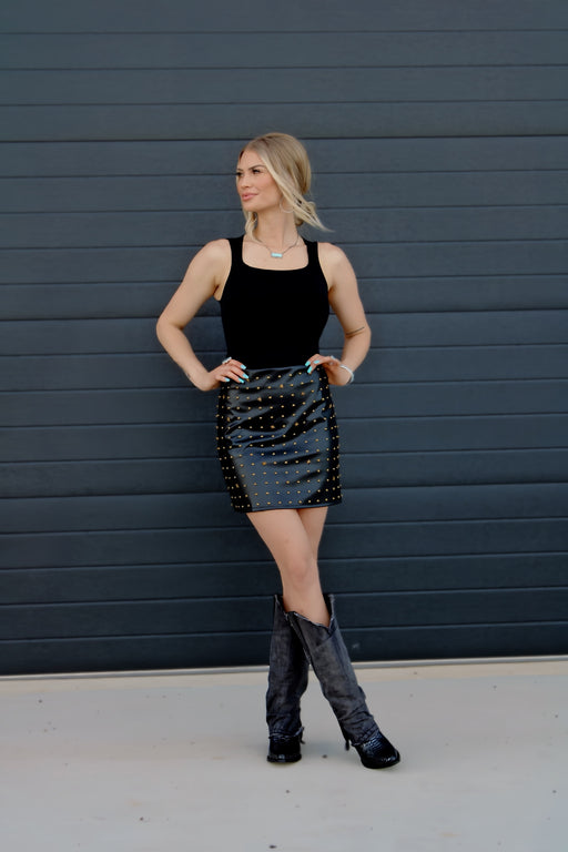 Woman wearing a black top and sequin skirt with black knee-high boots against a dark wall.