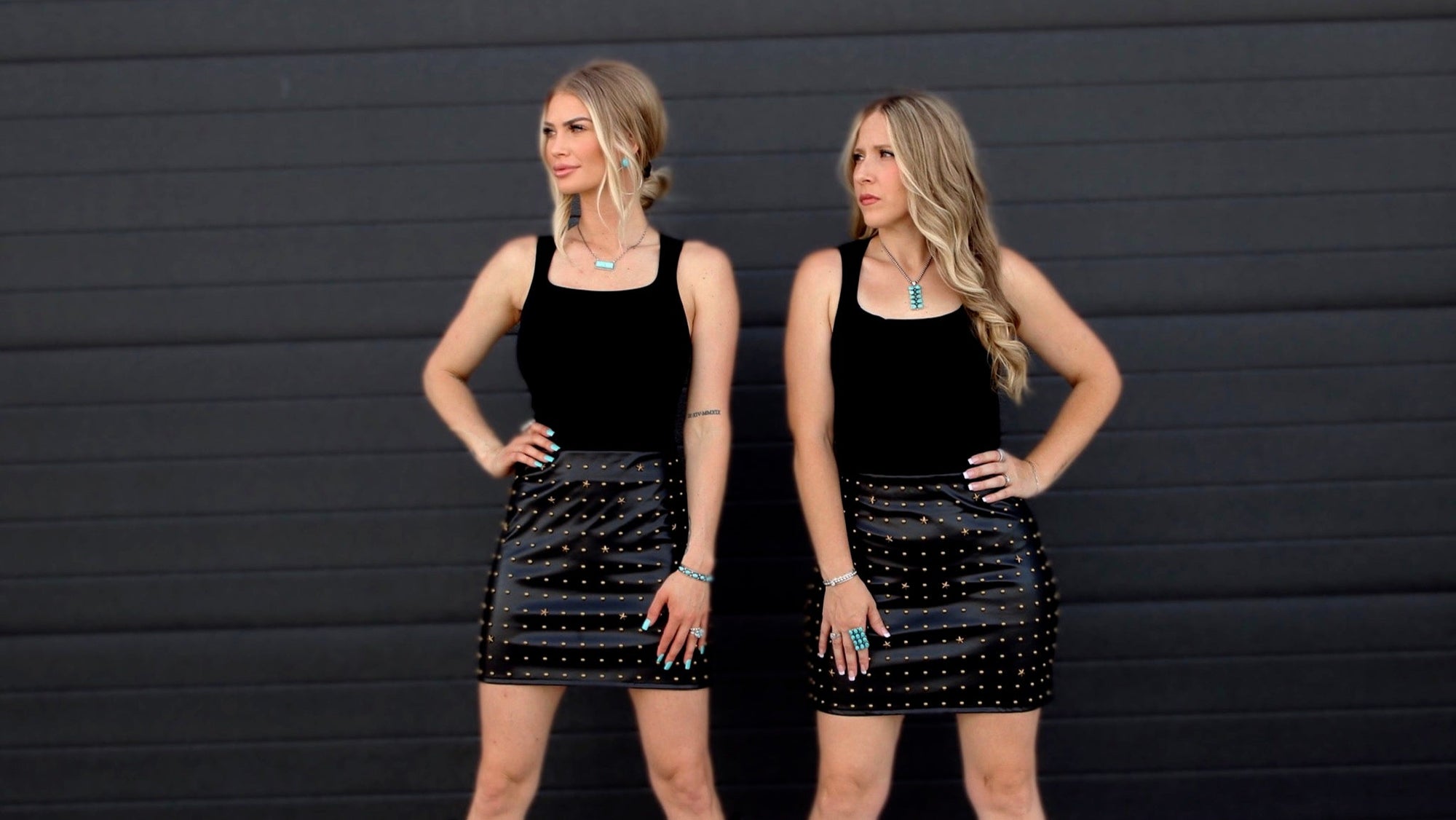 Two women wearing black outfits with studded details against a black background