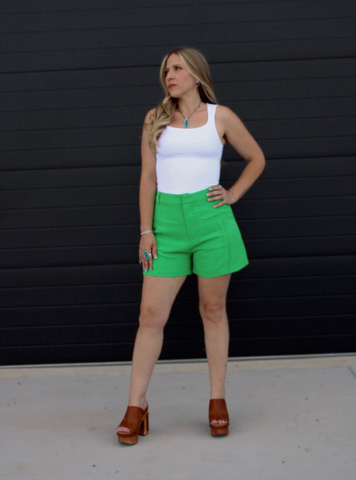 Woman wearing a white tank top and green shorts against a black background