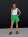 Woman wearing a white tank top and green shorts against a black background