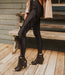 Person wearing black fringed leggings and boots on a wooden deck.