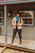 Woman in cowboy hat and boots standing on a wooden porch with a rustic building in the background