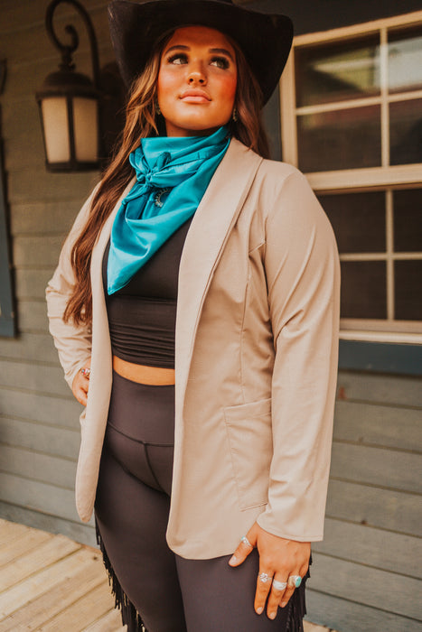 Woman wearing a beige cardigan, black top, and blue scarf standing in front of a building.