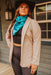 Woman wearing a beige cardigan, black top, and blue scarf standing in front of a building.